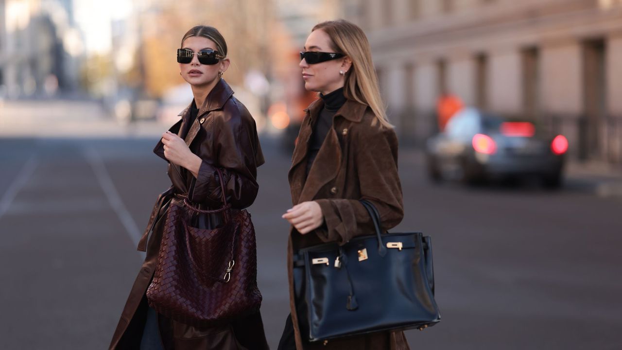 Two women crossing the street wearing brown trench coats with a clean-girl aesthetic, fitting for a powdery perfume look