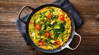 Omelette with tomatoes and greens on black pan from above