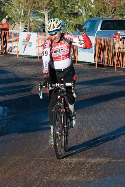A tired Dan Norton crosses the finish line can only manage a one hand salute as he collects the stars-and-stripes in the Master men's 60-64 race.