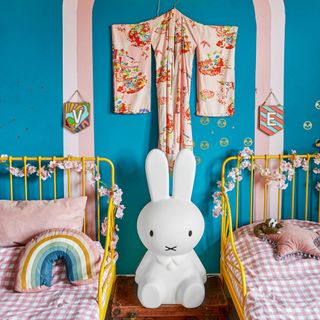 Blue twin bedded girl's bedroom with yellow metal beds and pink kimono on wall