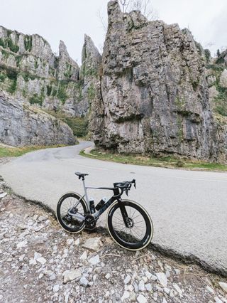 An aero bike with deep wheels stands on a hairpin within a steep sided gorge.