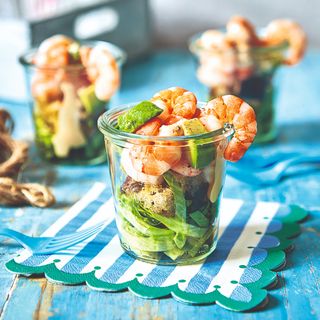 A glass pot filled with prawns and salad set on top of a striped paper napkin with a scalloped edge