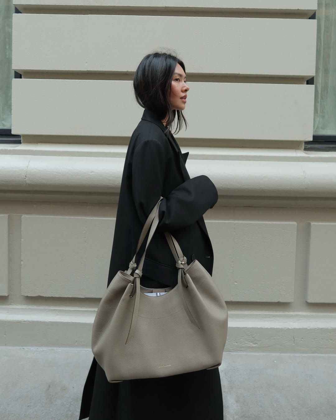 Influencer Mimi Xn holding a beige tote bag and black coat.
