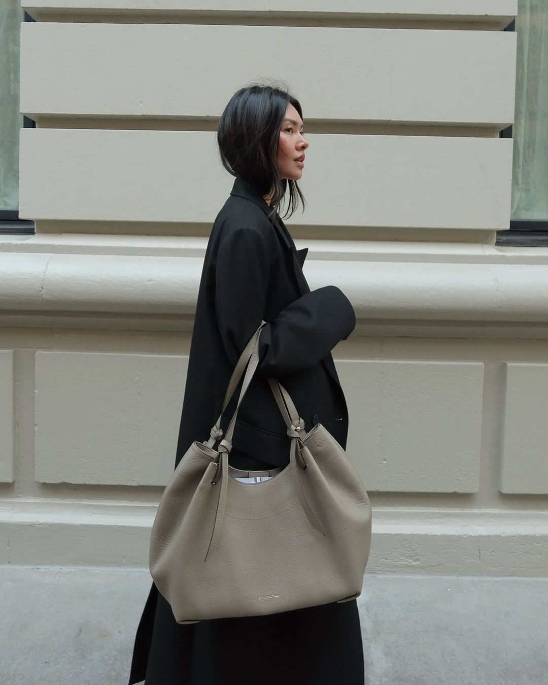Influencer Mimi Xn holding a beige tote bag and black coat.