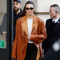 Kendall Jenner wears black trousers and a leather blazer.