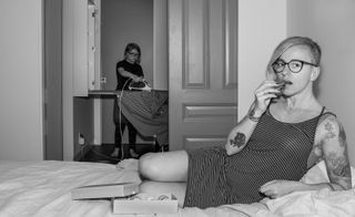 photograph of tattooed woman on bed and another woman ironing