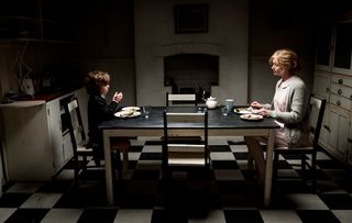 Samuel (Noah Wiseman) and his mother Amelia (Essie Davis) sit at a table in The Babadook, one of the best horror movies that are 95% and up on Rotten Tomatoes