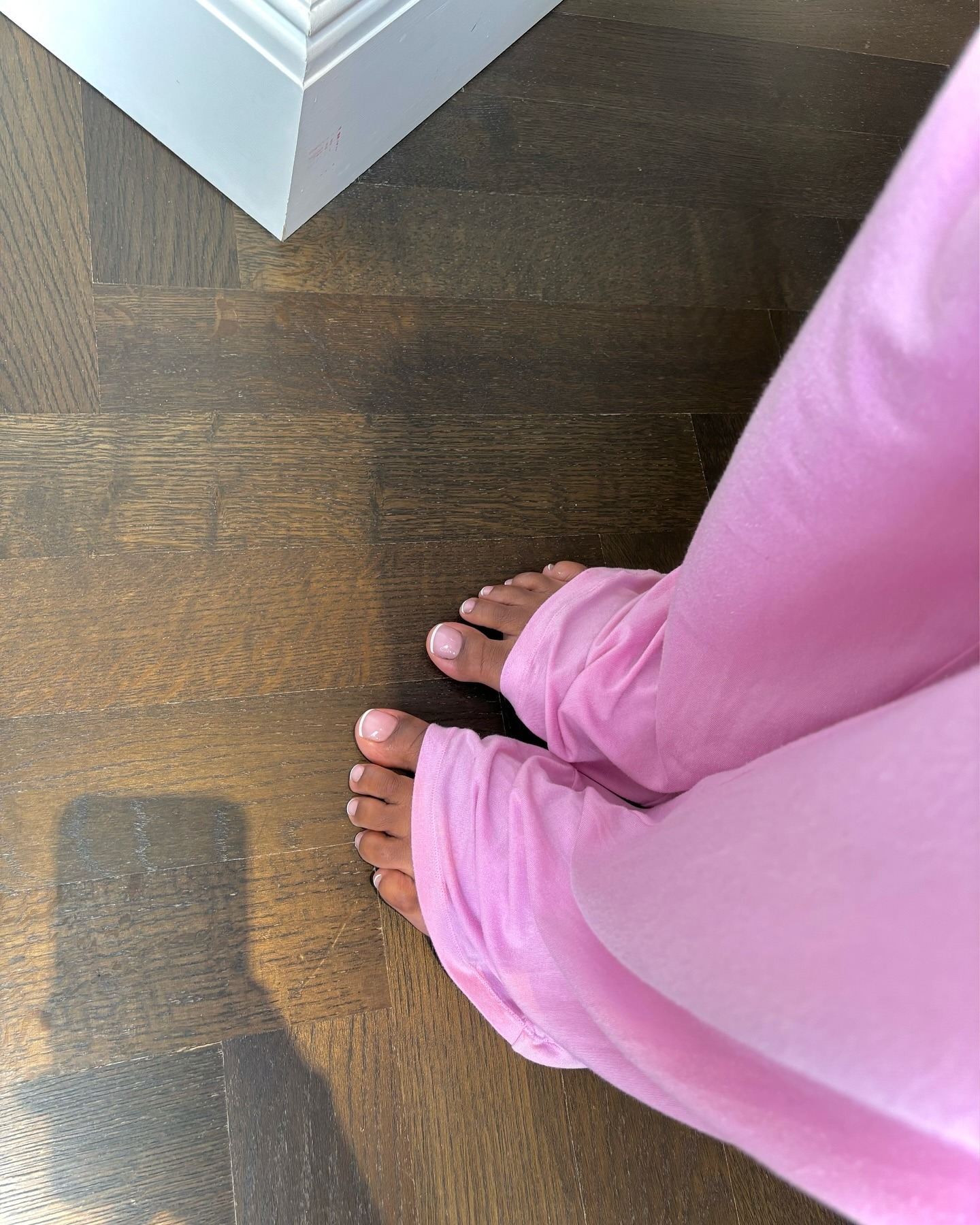 A woman wearing pink pyjama trousers with a shiny French tip pedicure