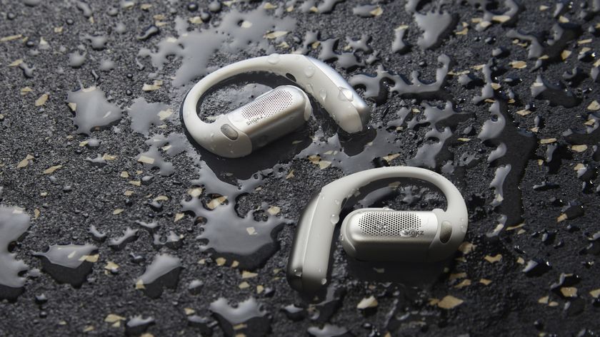 Press photo of the Shokz OpenFit Pro earbuds sitting on a wet surface, with water droplets visible on the earbuds.