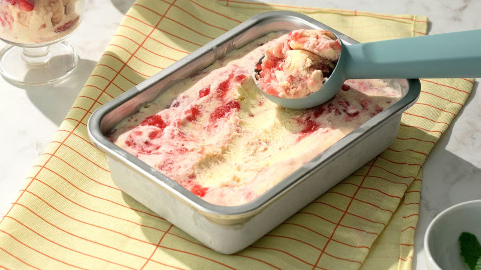 A small rectangular stainless steel food container filled with ice cream with a scoop on top 