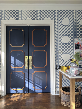 French doors with gold trim in room with patterned blue wallpaper and hardwood floors
