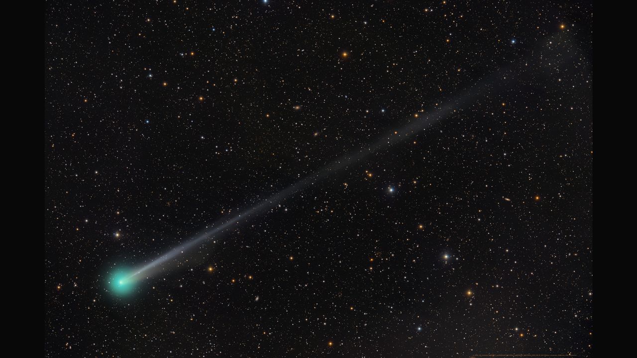 A bright green comet is pictured to the bottom left of a starfield against a black sky, with a long tail extending to the upper right of the screen.