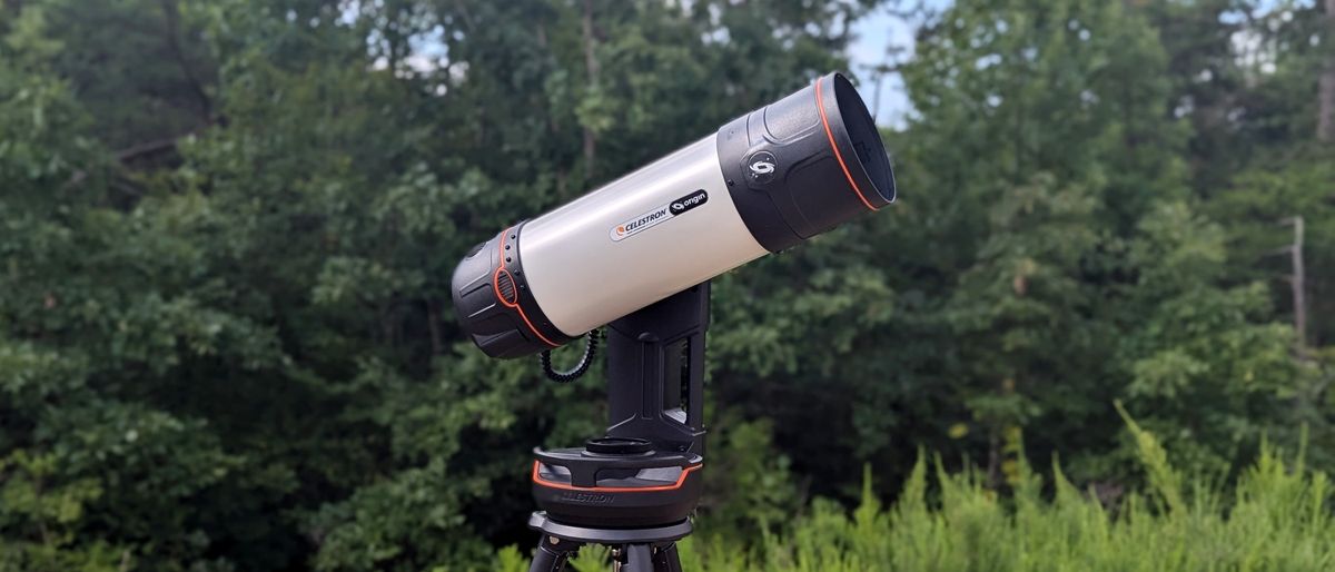 a black and white telescope in a field with trees behind it