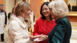 Geri Horner wearing an ivory jacket talking to Queen Camilla as a woman in a red dress looks on