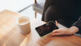 A person in a coffee shop holding a phone displaying the low battery symbol