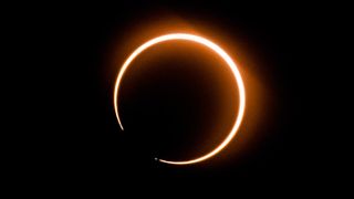 During an annular solar eclipse a broken ring of orange golden light is seen against a black background.