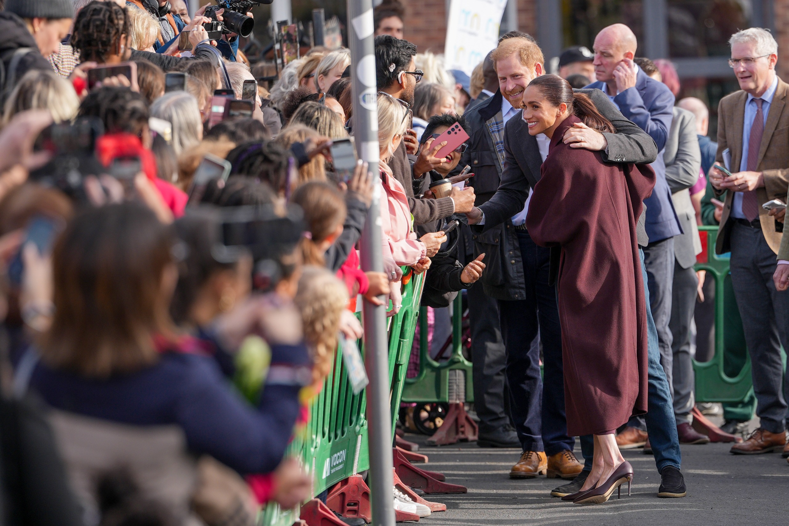 Prince Harry hugging Meghan Markle standing in front of a crowd of fans