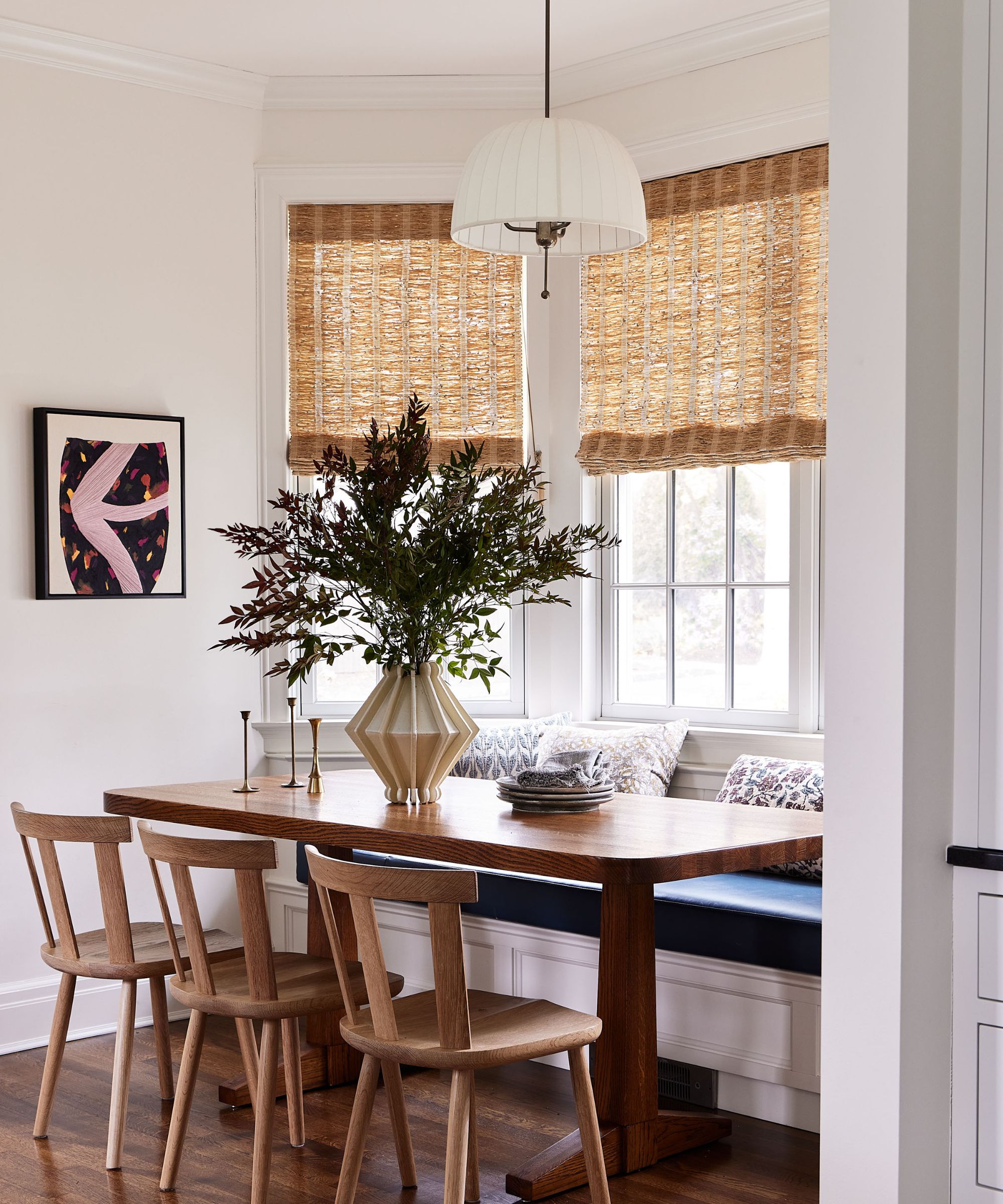 Breakfast nook with wood table and chairs, rattan blinds, built-in storage bench and vase with flowers