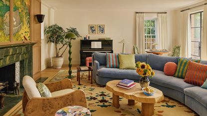 a warm neutral london living room centered around a large fireplace with large artwork hung above. a blue curved couch sits to the right, with a wooden coffee table and patterned rug 