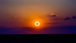 golden orange ring of fire during an annular solar eclipse, with a partly cloudy sky behind.