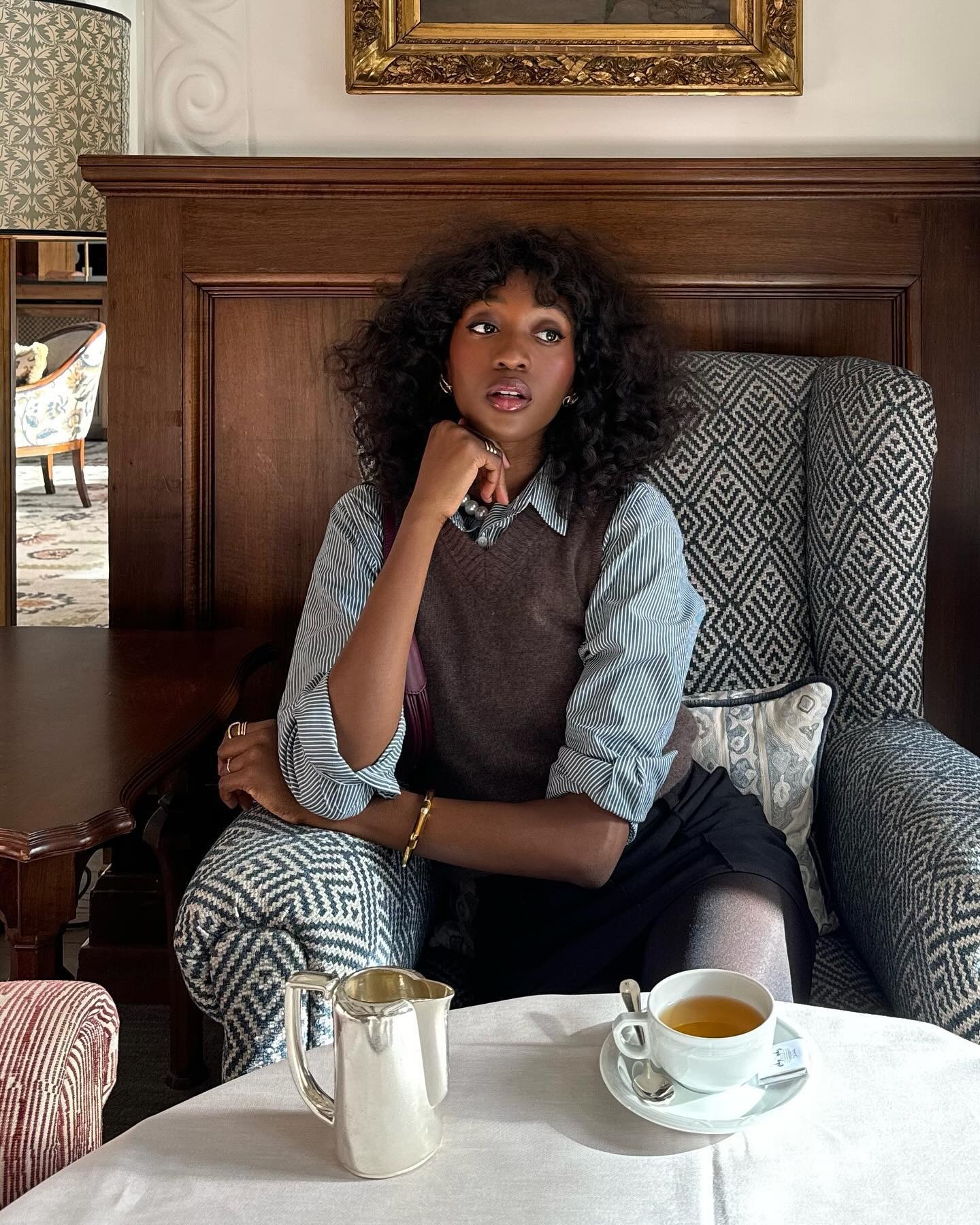 A woman in a plush chair with tea on the table.