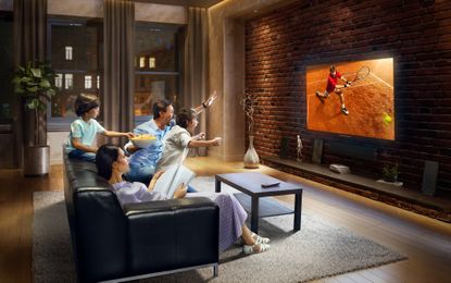 Father and two young children cheering and watching Tennis game on TV. Mother is reading a magazine. They are sitting on a sofa in the modern living room. The TV set is on the loft brick wall. It is evening outside the window.