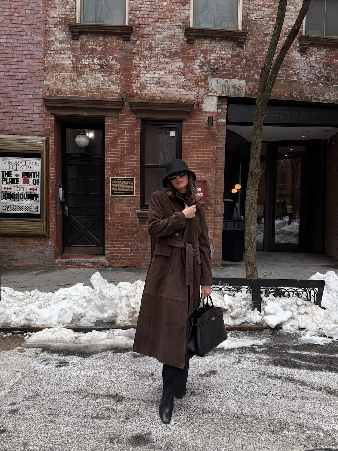 Kathryn Zahorak wearing black hat, brown coat, sunglasses, boots, black bag in new york city