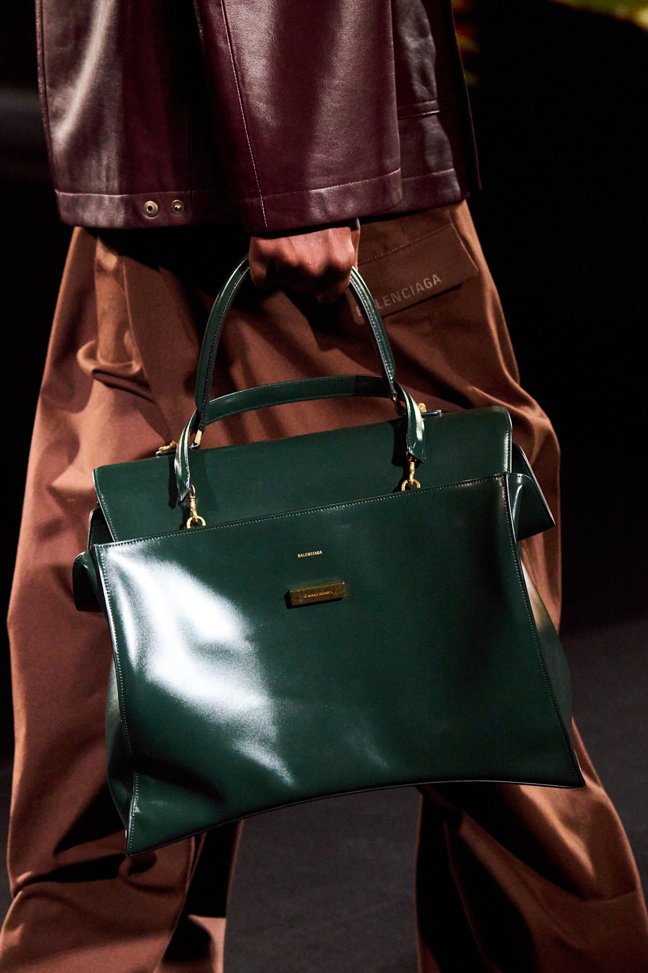 A close-up shot of a model walking in the Balenciaga F/W 26 show during Paris Fashion Week carrying a dark-green handbag.