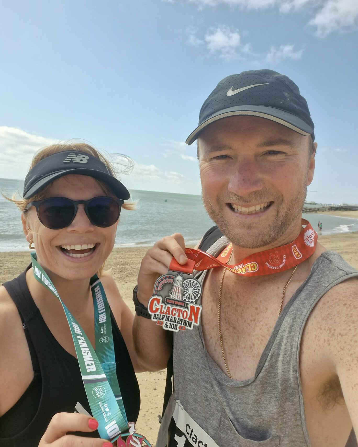 Woman and man stand with medals around their necks and the sea in the background