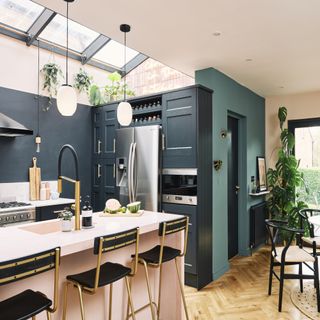 kitchen with a pink island, wooden flooring, grey cabinets, skylights, pendant lighting and black bar stools