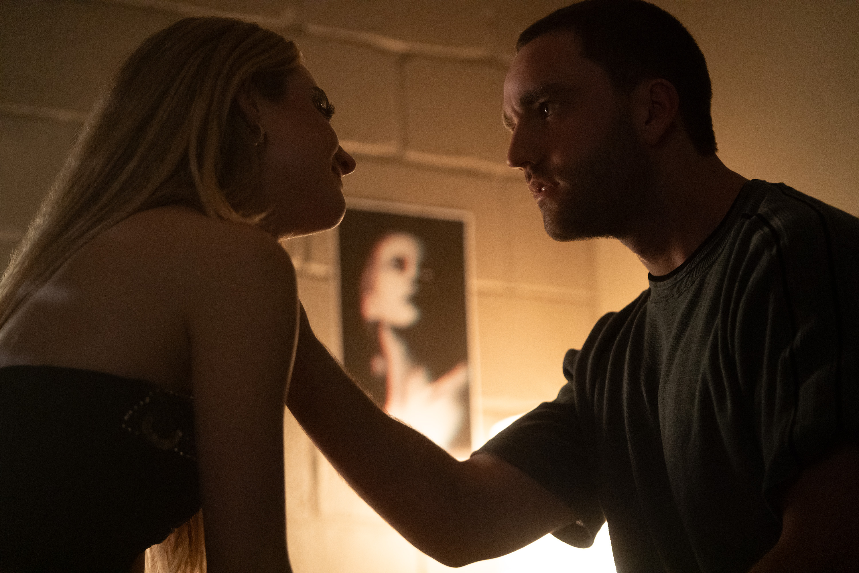 grace van patten as lucy smiling while jackson white as stephen puts his hand on her shoulder in a dorm room in tell me lies season 3