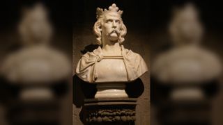 Bust of Robert the Bruce. He has curly, chin-length hair, thick eyebrows and a thick moustache. He is wearing a crown on top of his hair and what looks to be a cloak around his shoulders.