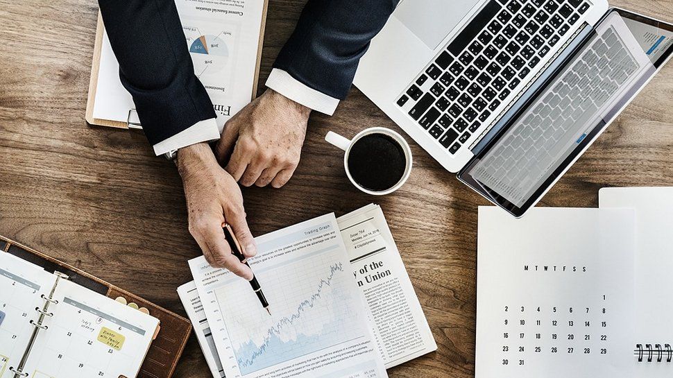 A person pointing at a graph on a business desk.