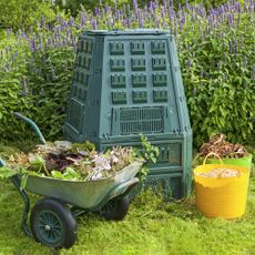 Home compost bin in the garden with wheelbarrow and buckets of composting ingredients