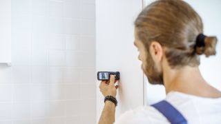 Man holding one of the best laser measures against a bathroom wall