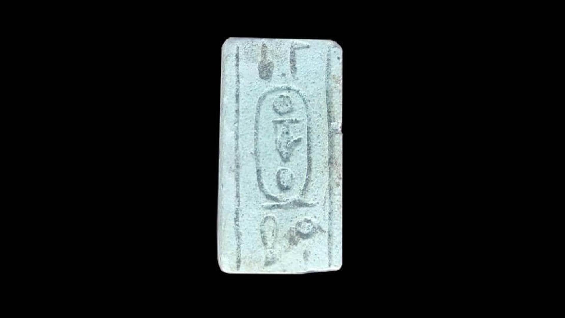 A photograph of a cartouche found in the rest house. It is made of light gray stone and has markings on it.