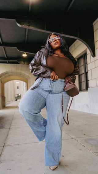 thamar wears wide-leg relaxed jeans, pointy heels, brown top and brown leather jacket