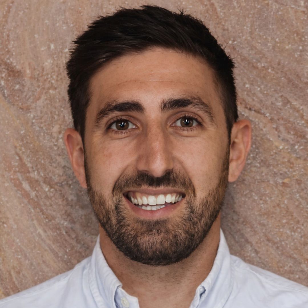 Headshot of a man with lack hair and a black beard smiling at the camera