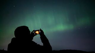 A photo of a person taking a photo of the Northern Lights on their phone