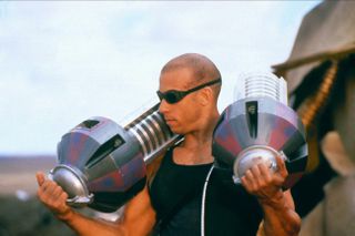 Vin Diesel as Richard B. Riddick, holding two massive cannisters on his shoulders in Pitch Black