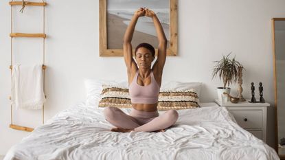 Yoga for sleep, woman in a seated position on a bed with her arms above her head
