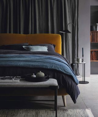 Bed with orange headboard and blue bedding with a bench positioned at the bottom of the bed.