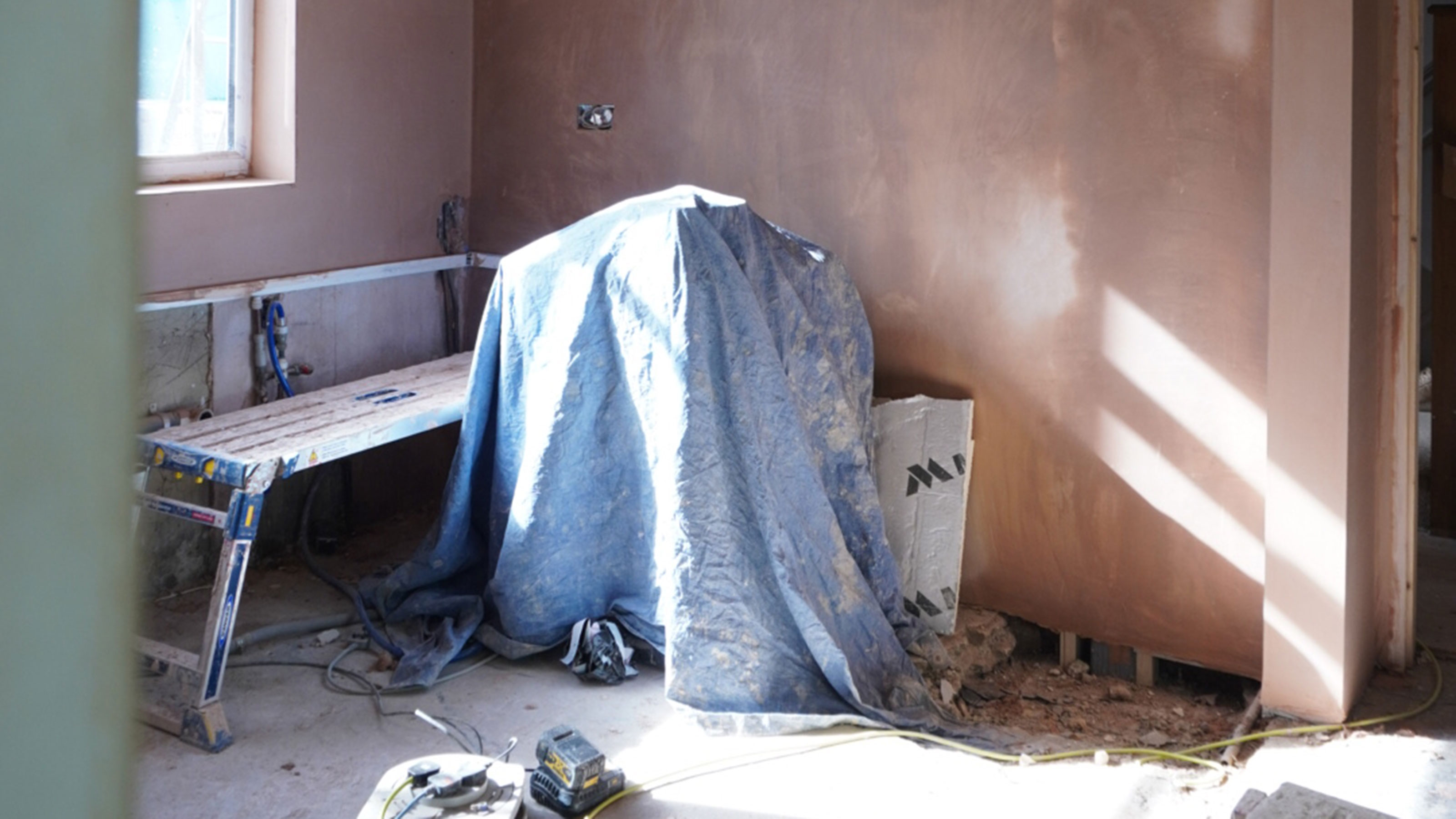 Room mid renovation with plastered walls and paint-splattered bench