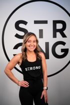woman facing the camera smiling wearing a black vest with strong written on it