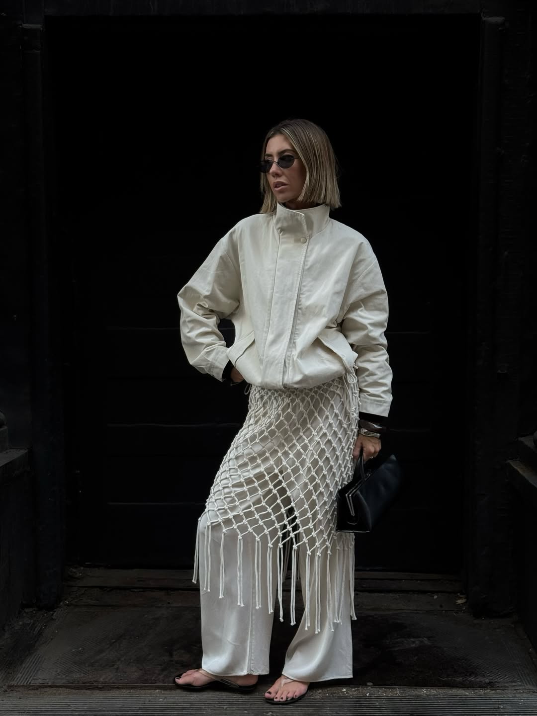Hannah in white trousers, technical jacket and neutral flip-flops