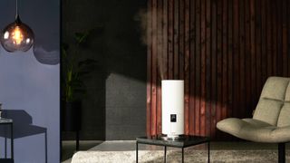 white humidifier on black coffee table in living room with dark wooden panelling, blue wall, padded armchair and hanging glass pendant light
