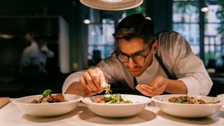 chef in restaurant applying garnishes to dishes