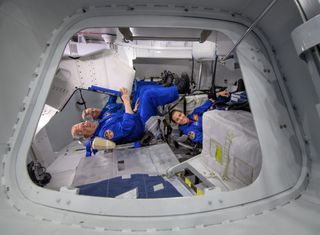 NASA astronaut Eric Boe (top foreground), Boeing astronaut Chris Ferguson (top background) and NASA astronaut Nicole Aunapu Mann sit inside a mockup of a Boeing CST-100 Starliner spacecraft. The three astronauts form the test flight crew for Boeing's first crewed Starliner flight in 2019.