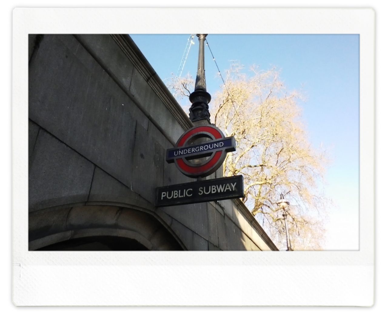 A sign for the London Underground in a bridge in front of a blue sky