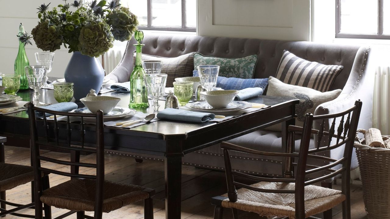 Wood dining table with white crockery, green glassware and a grey banquette